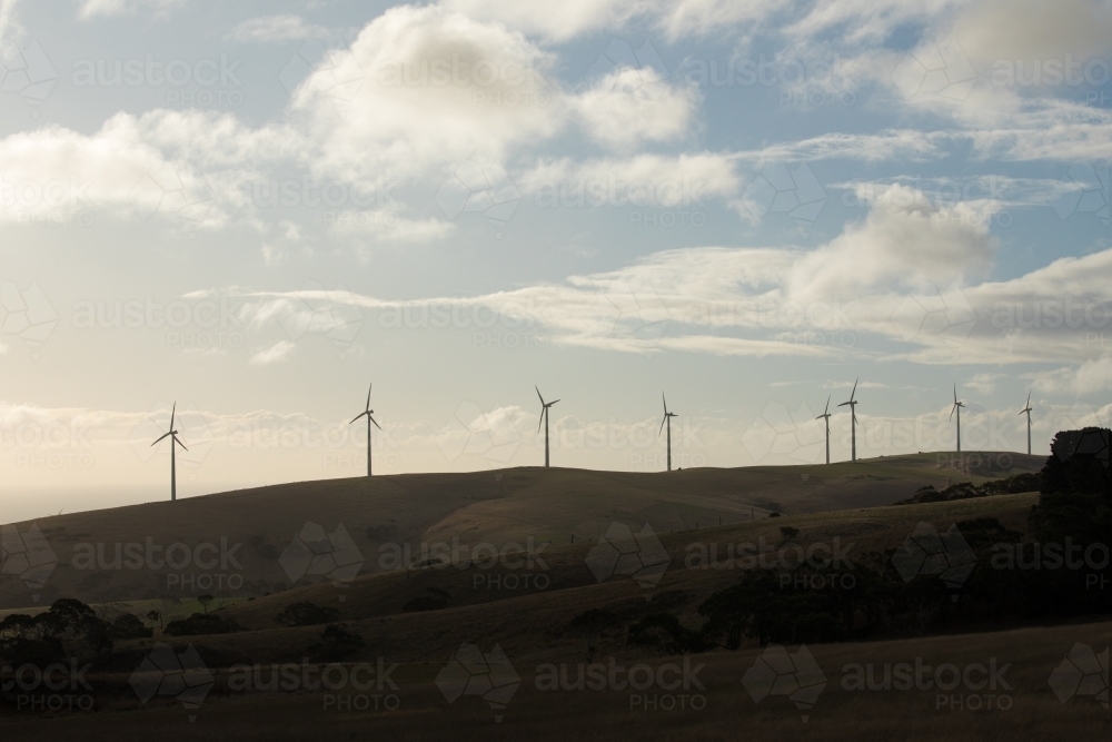 Silhouetted row of wind turbines on a hill in a paddock - Australian Stock Image