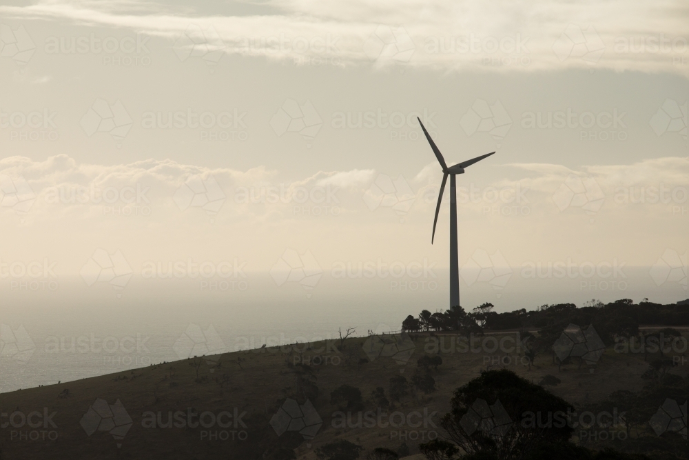 Silhouetted wind turbine on a hill in a paddock - Australian Stock Image