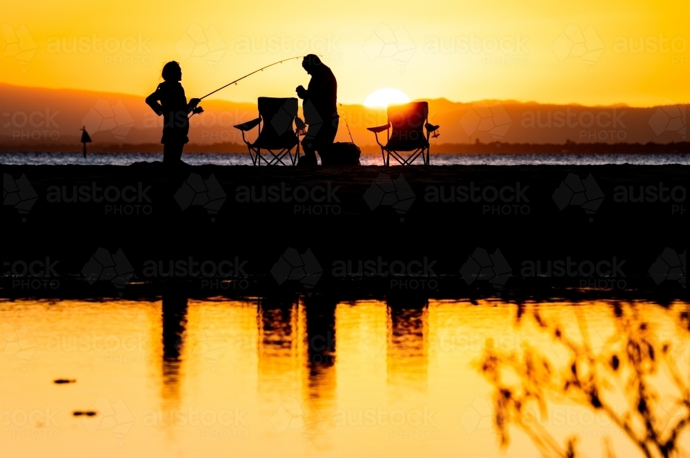 silhouettes of people fishing on the beach at sunset - Australian Stock Image