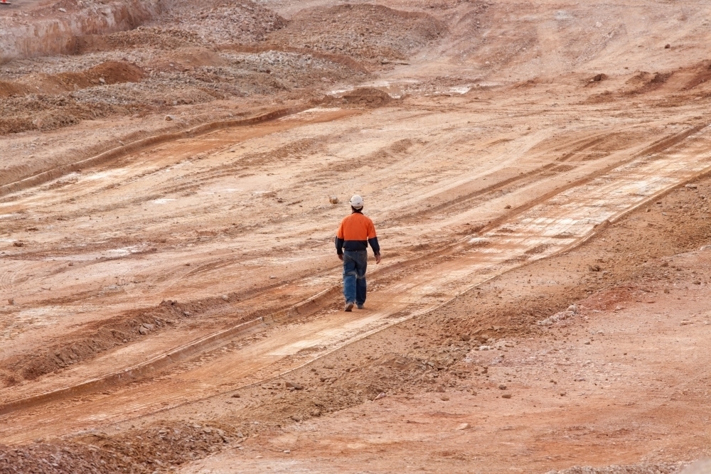 Single construction worker walking across a large industrial building site - Australian Stock Image