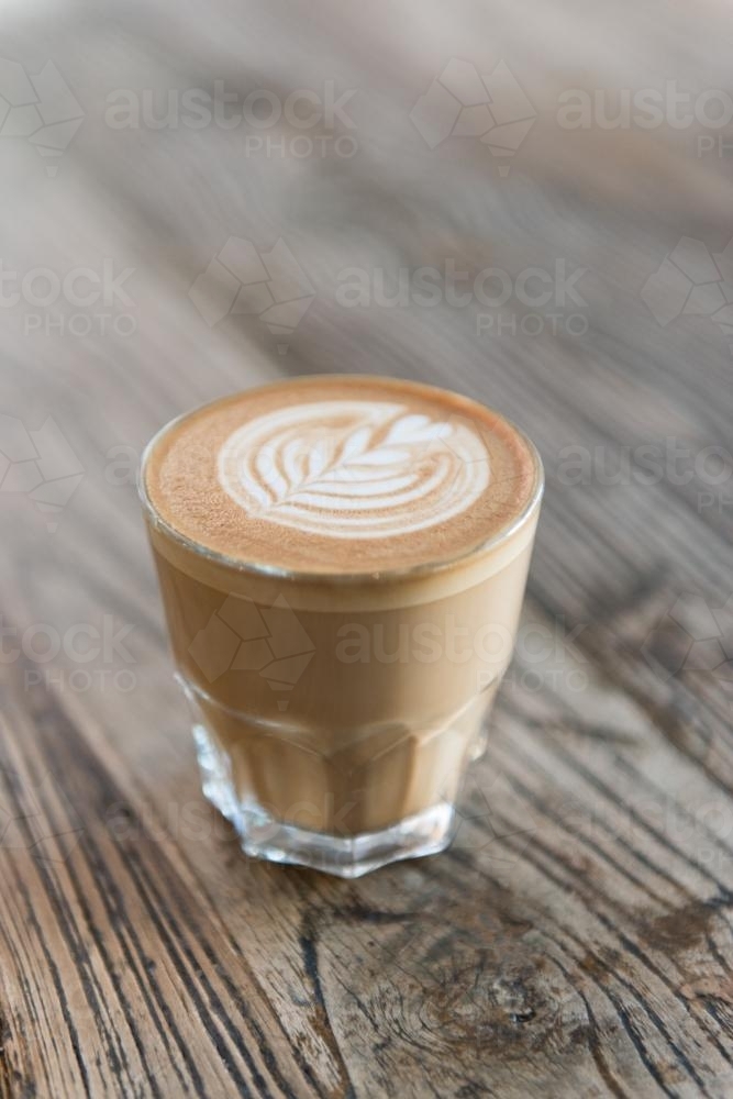 Single latte coffee sitting on a wooden table - Australian Stock Image