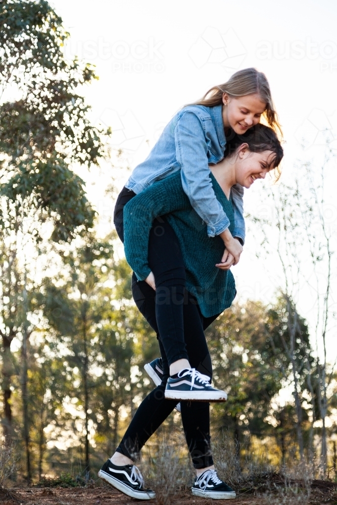 Sister giving her younger sibling a piggyback ride - Australian Stock Image