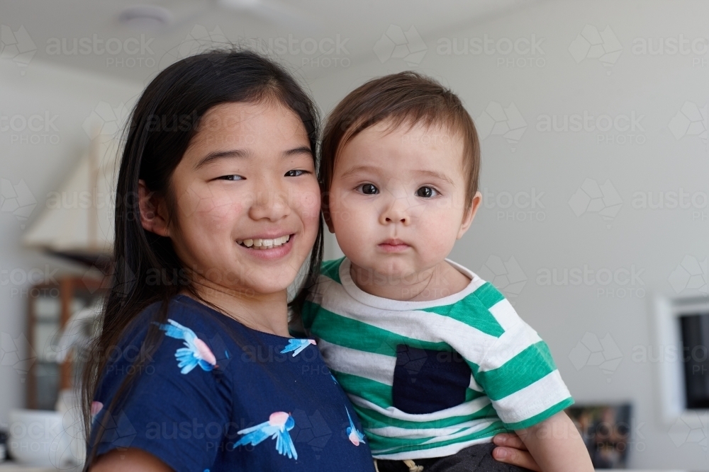 Sister holding younger baby brother in kitchen - Australian Stock Image