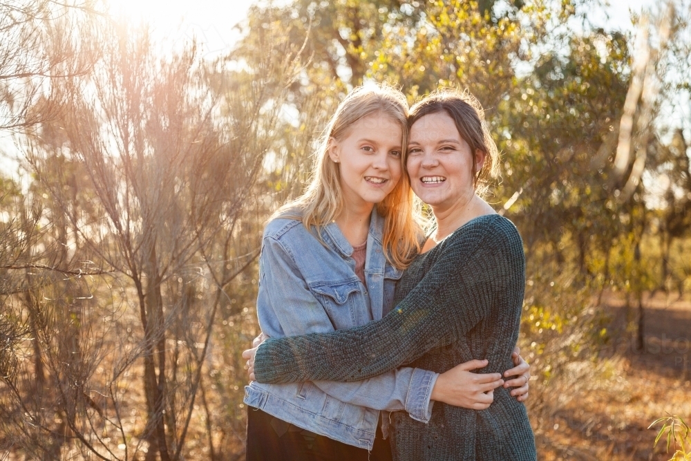 Sisters laughing together and giving one another a hug - Australian Stock Image