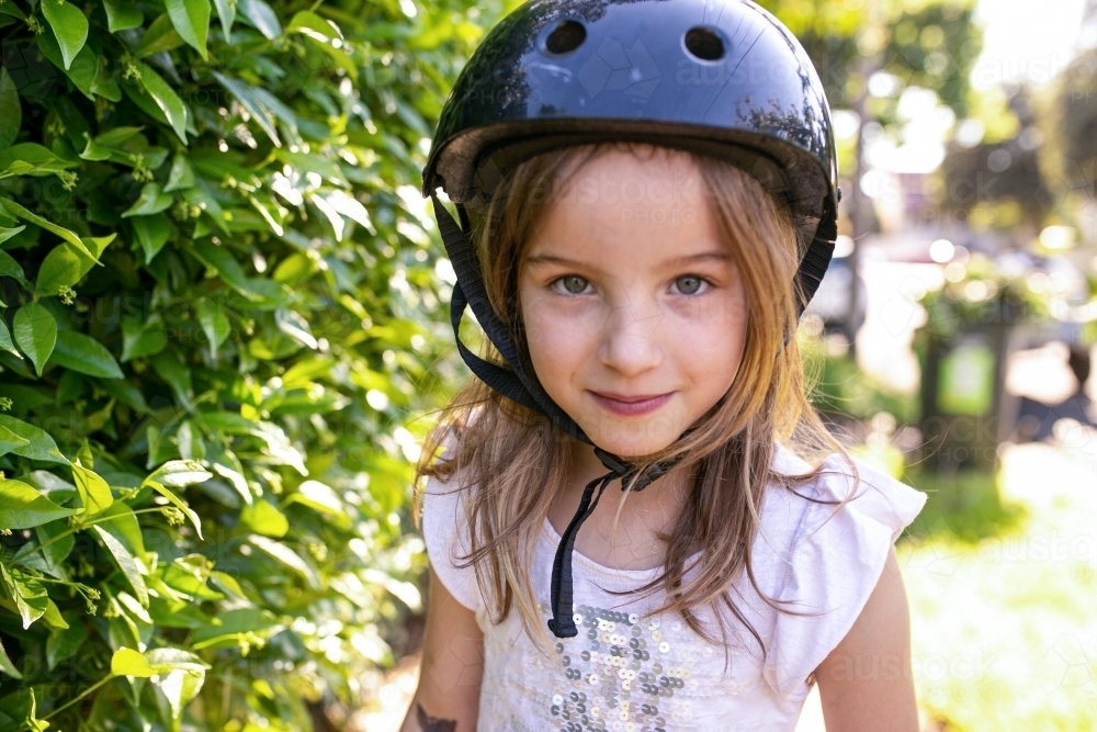 Close up shot of a smiling blonde girl with black helmet and hedge on the side on a sunny day - Australian Stock Image