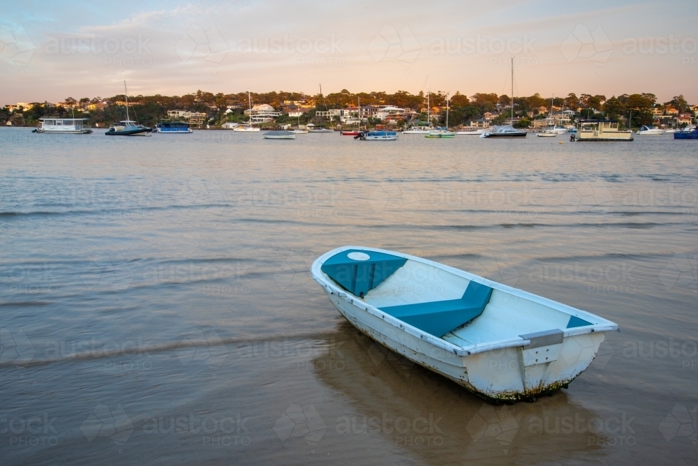 Small boat on sand flats with incoming tide at sunrise - Australian Stock Image