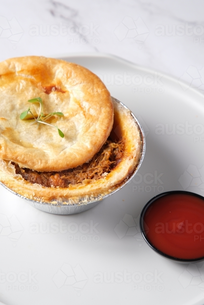 Small open meat pie with side of tomato sauce - Australian Stock Image