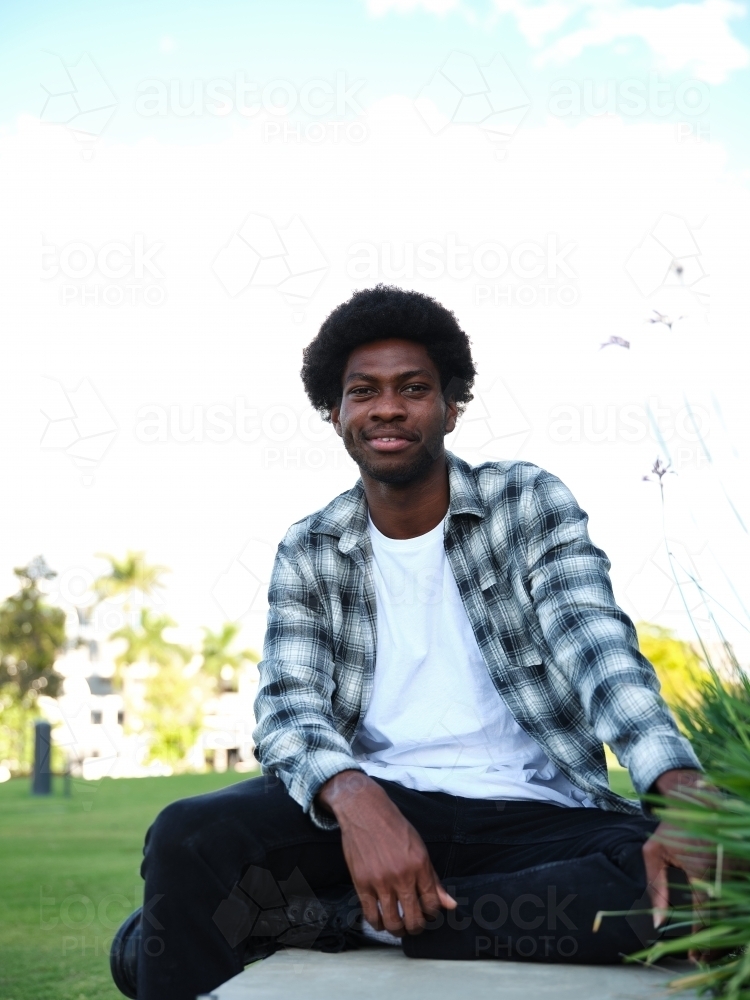 Smiling man sitting on a concrete park bench wearing a checkered polo shirt - Australian Stock Image