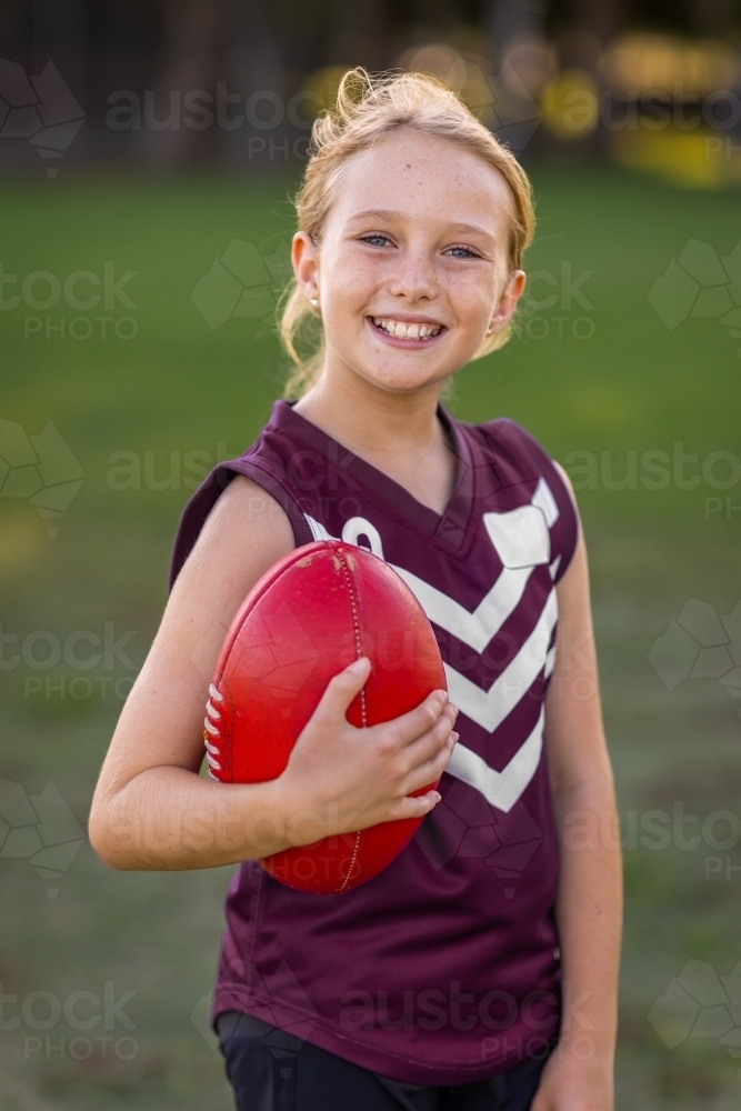 smiling blonde girl looking at camera and holding a football - Australian Stock Image