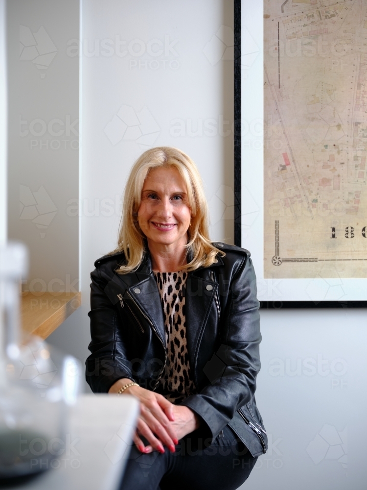 Smiling blonde middle aged woman wearing leopard print and leather jacket with hands overlapped - Australian Stock Image