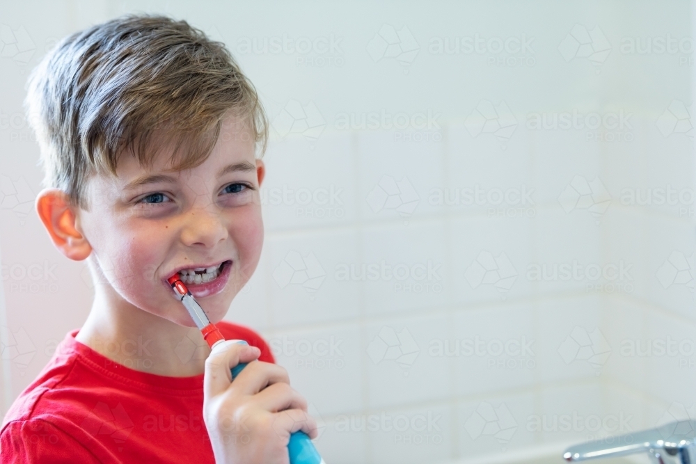 Smiling boy using electric toothbrush - Australian Stock Image