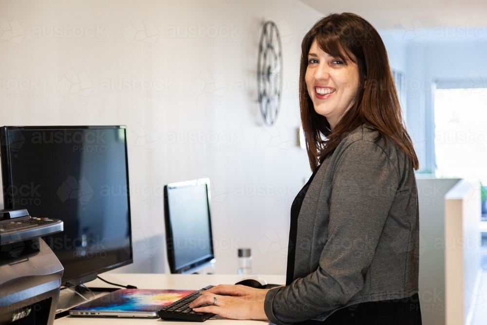 Smiling businesswoman standing at stand up desk in home office - Australian Stock Image