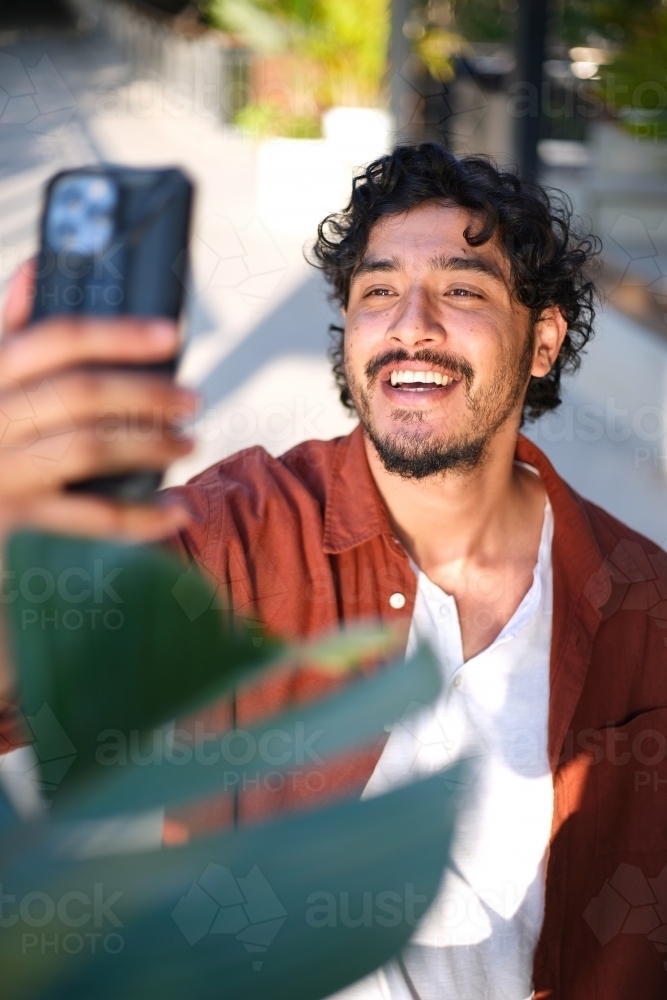 Smiling curly haired man taking a selfie with his mobile phone - Australian Stock Image