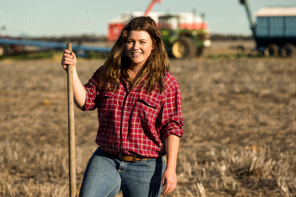 Smiling female farmer standing in agricultural field with rake - Australian Stock Image