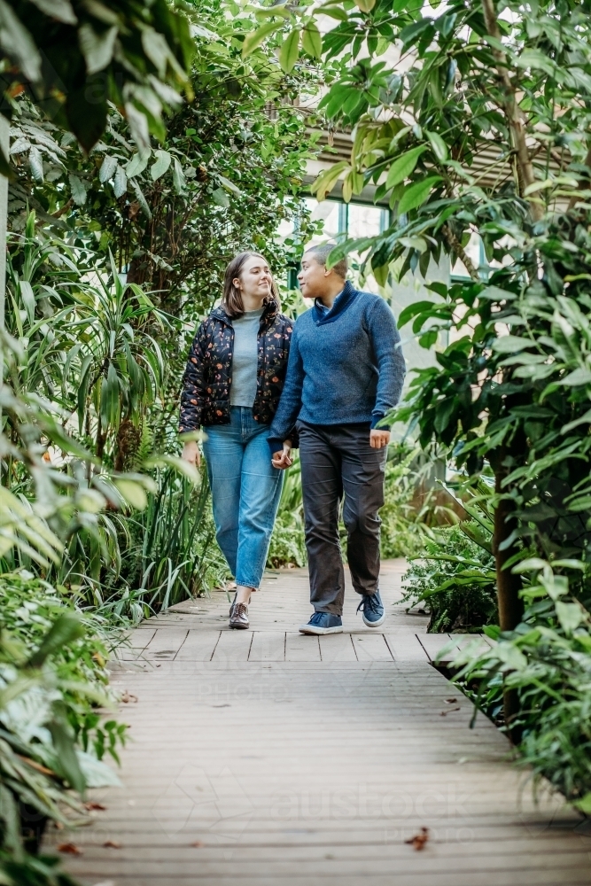 smiling lgbtqi couple holding hands while looking at each other walking in a garden - Australian Stock Image