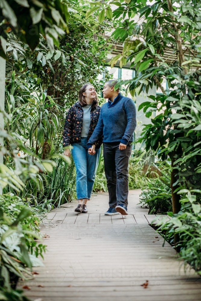 smiling lgbtqi couple holding hands while looking at each other walking in a garden - Australian Stock Image