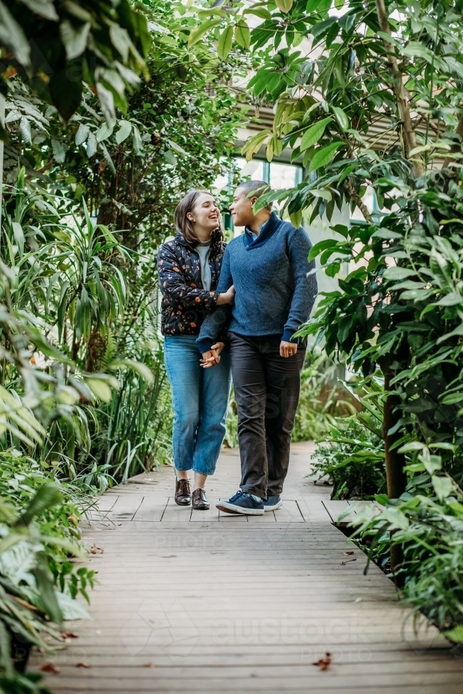 smiling lgbtqi couple holding hands while looking at each other walking in a garden - Australian Stock Image