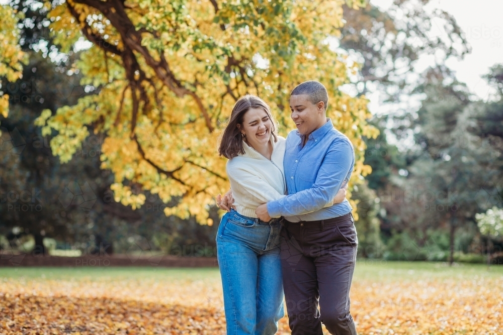 smiling lgbtqi couple hugging each other by the autumn trees - Australian Stock Image