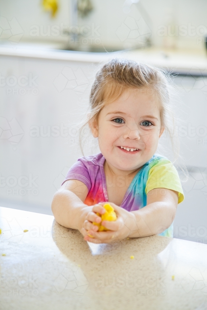 Smiling little kid making things with playdough in kitchen - Australian Stock Image