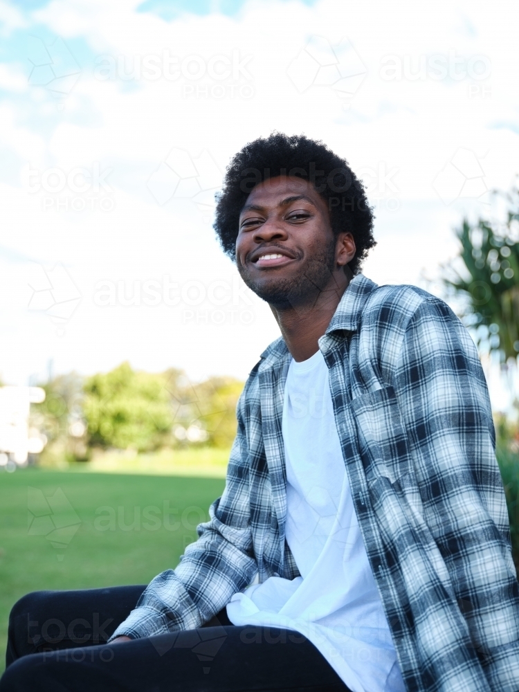 Smiling man sitting on a concrete park bench wearing a checkered polo shirt - Australian Stock Image