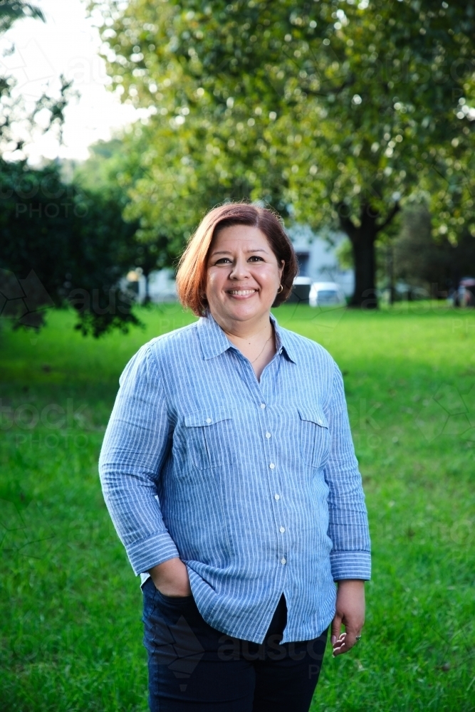 Smiling middle aged woman with short hair wearing blue and white striped shirt - Australian Stock Image