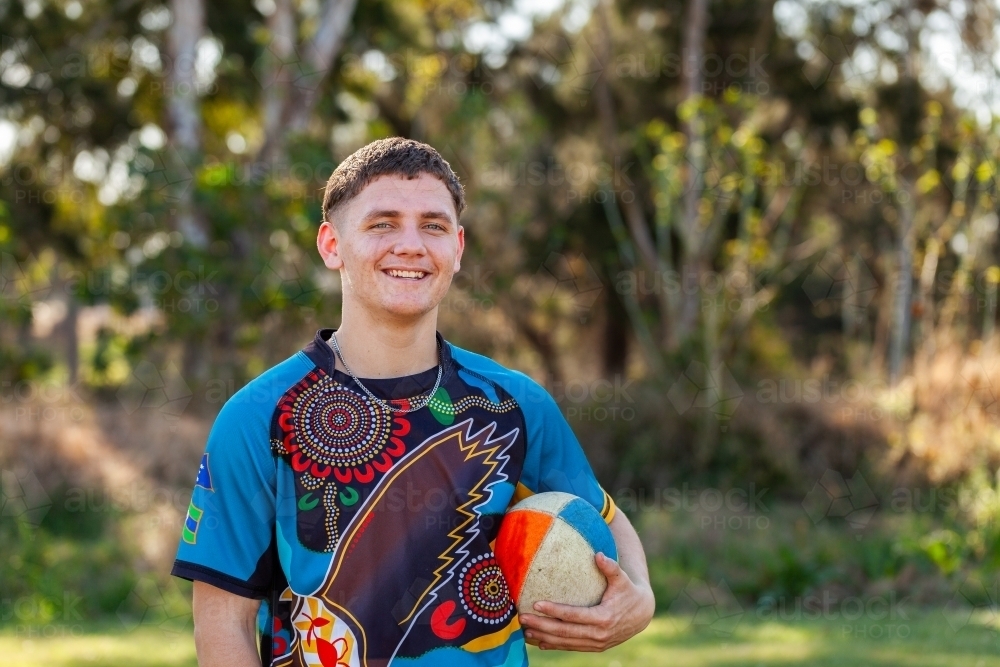 Smiling portrait of happy teenage Australian footy sports player holding football - Australian Stock Image