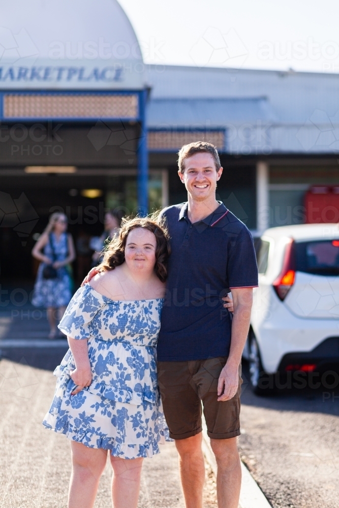 Smiling portrait of teen girl with down syndrome in community near shops with her provider - Australian Stock Image