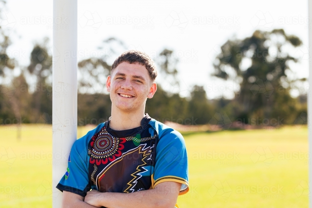 Smiling portrait of teenage aboriginal footy player leaning on goal post - Australian Stock Image