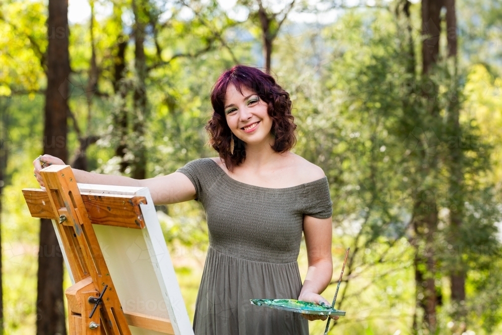 Smiling portrait of young australian artist standing beside canvas on easel - Australian Stock Image