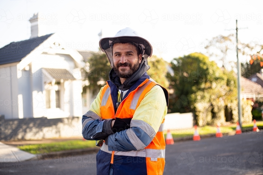 Smiling road worker man with beard wearing high vis jacket with his arms crossed - Australian Stock Image