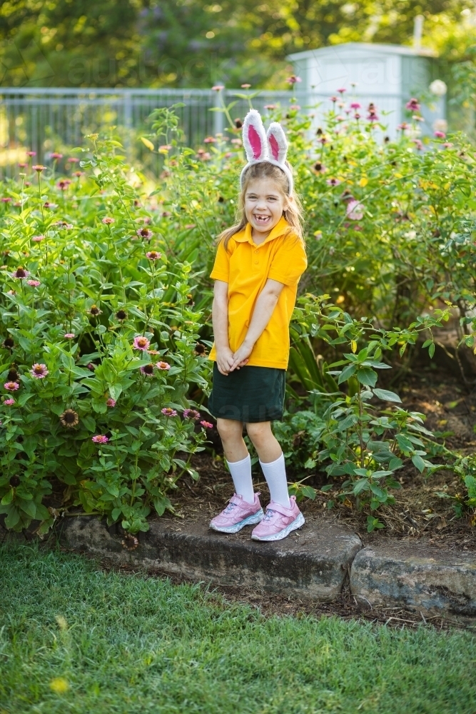 Smiling school kid outside in garden wearing rabbit ears for Easter celebrations - Australian Stock Image