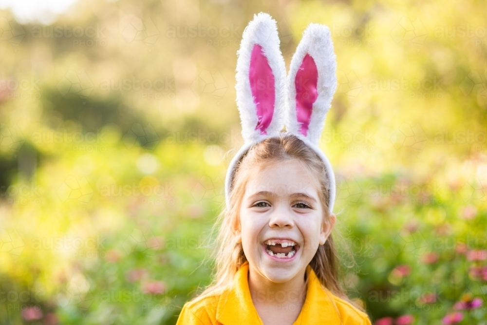 Smiling school kid outside in garden wearing rabbit ears for Easter celebrations - Australian Stock Image