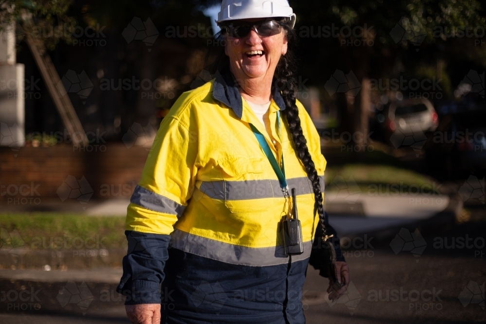 Smiling traffic controller woman wearing white helmet and yellow jacket with long hair braided - Australian Stock Image