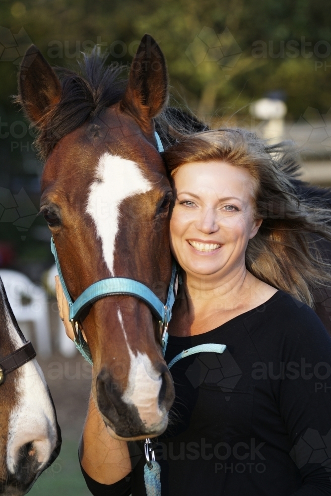 Smiling woman holding horses head - Australian Stock Image