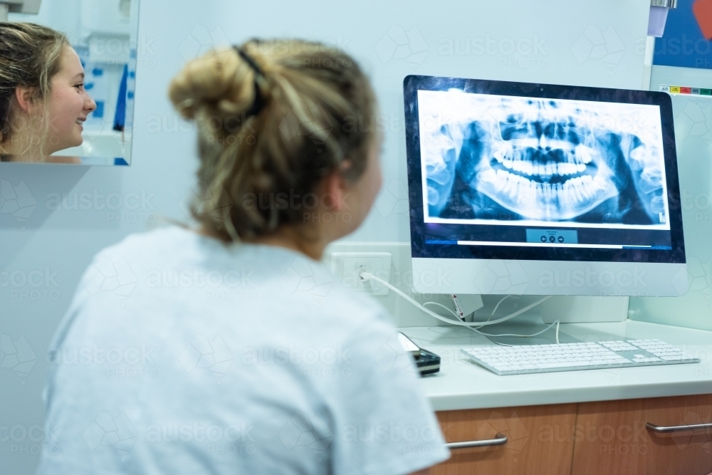 Smiling woman looking at dental X-ray on computer monitor - Australian Stock Image