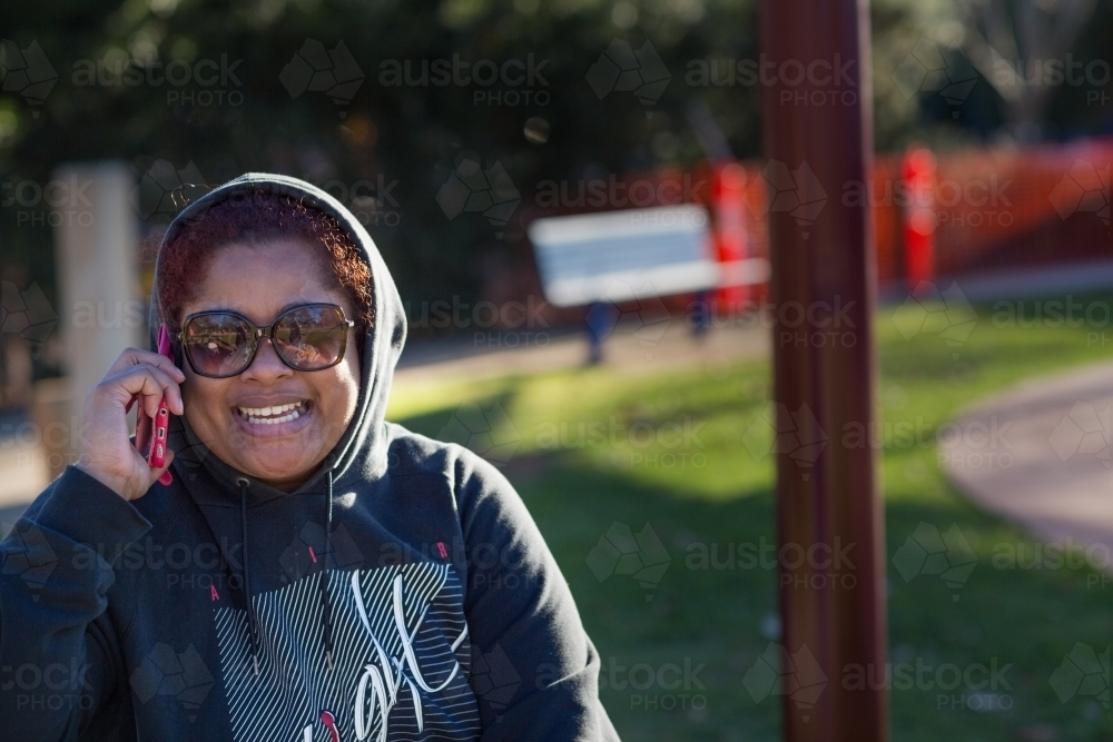 Smiling woman wearing hoody and sunglasses talking on phone - Australian Stock Image