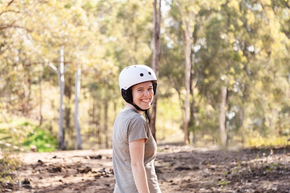 Smiling woman with horse riding helmet on looking back over her shoulder - Australian Stock Image