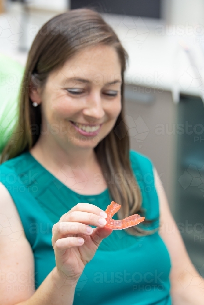 Smiling women holding and looking at dental splint - Australian Stock Image