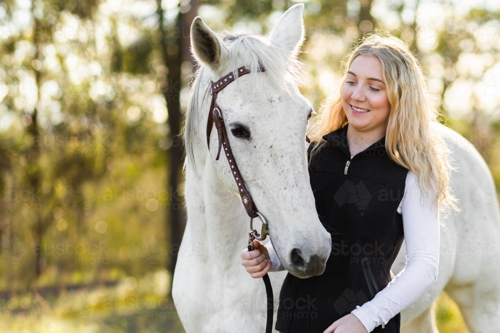 Smiling young adult horse lover with her pony in warm light - Australian Stock Image