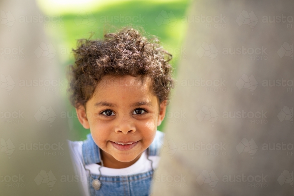 smiling young child looking up through gap - Australian Stock Image