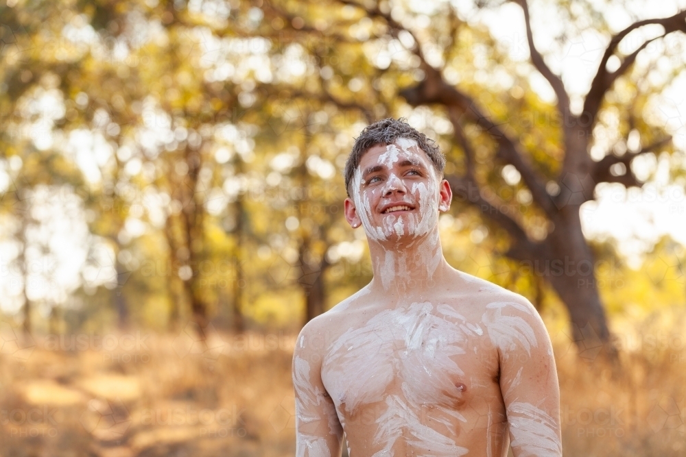 Smiling young first nations Australian man looking up with bokeh bushland backdrop - Australian Stock Image