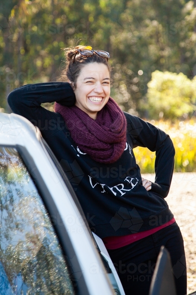 Smiling young person leaning on side of car in winter - Australian Stock Image