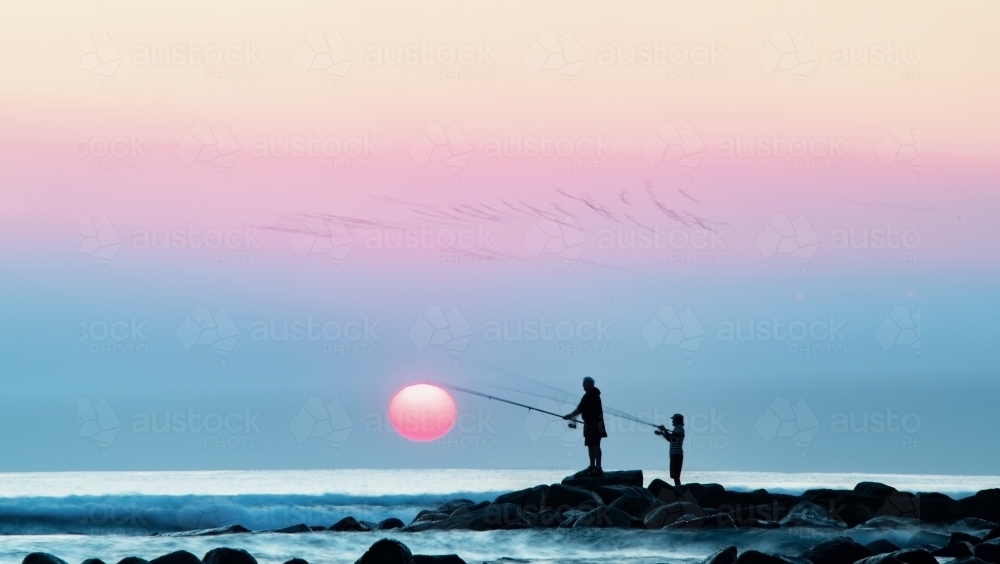 Smokey hazy over the coast while fishermen fish next to rising sun. - Australian Stock Image