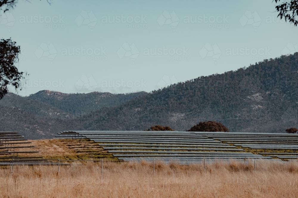 Solar farm panels on a hill for renewable energy with mountains in the background. - Australian Stock Image