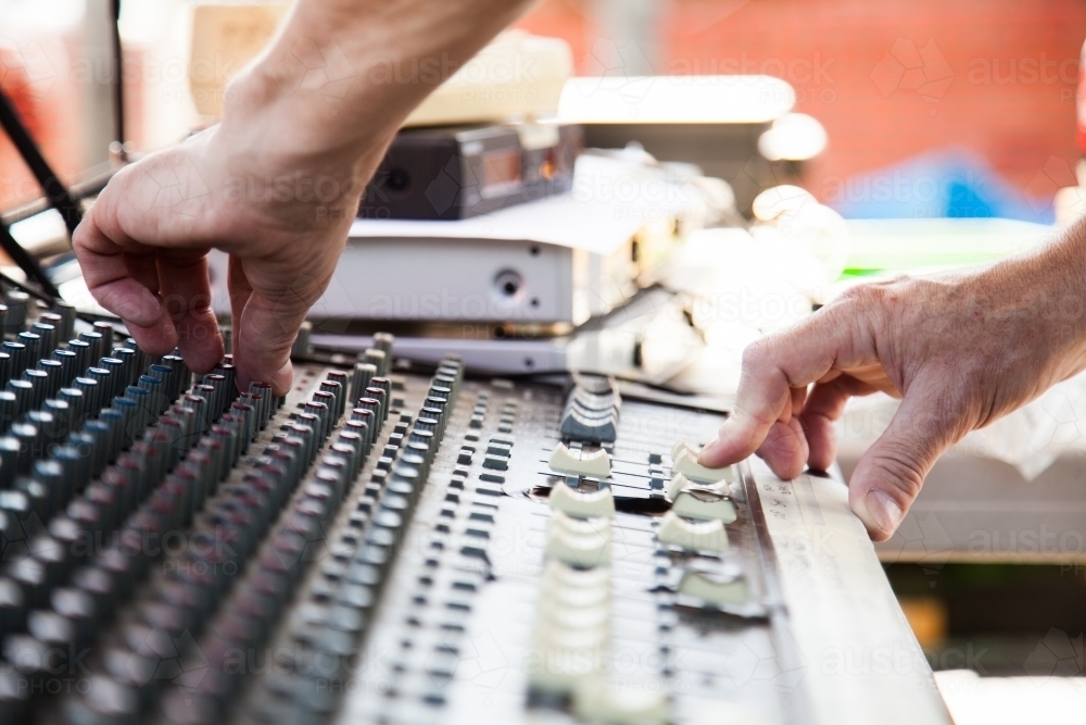 Sound guy turning knobs on a sound system audio mixer - Australian Stock Image