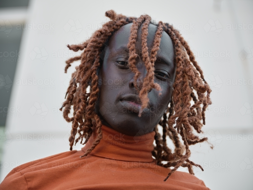 South Sudanese man wearing orange turtleneck looking down - Australian Stock Image