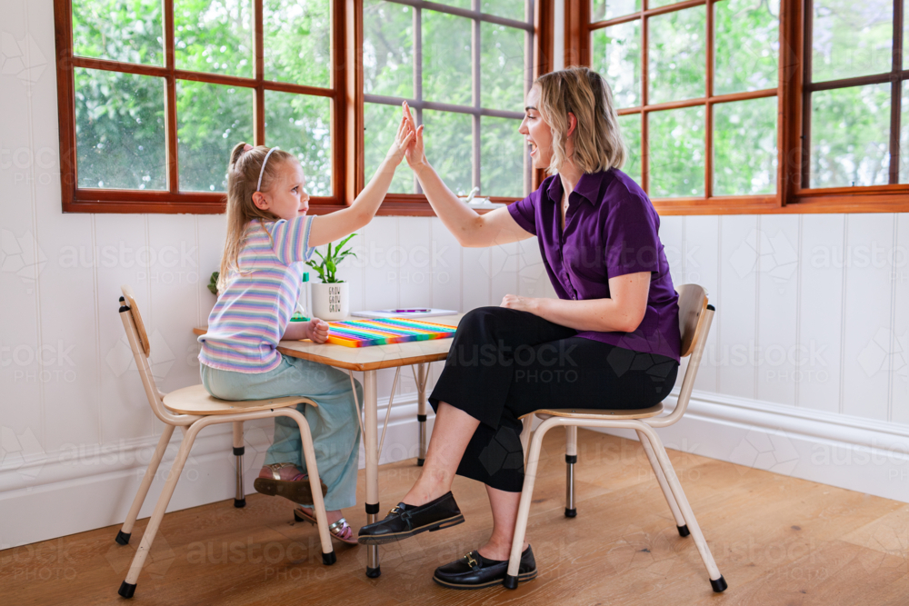 Speech therapist professional with child in clinic high five together to celebrate success - Australian Stock Image