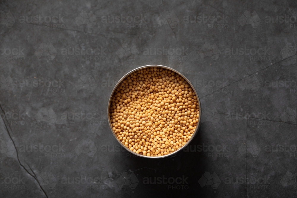 Spice tin of yellow mustards seeds on dark marble background - Australian Stock Image