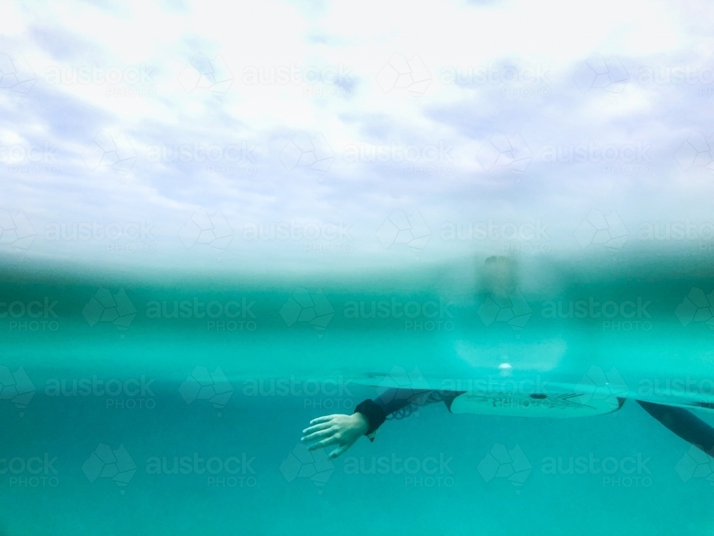 Split image of Arms paddling on boogie board underwater and overcast sky - Australian Stock Image