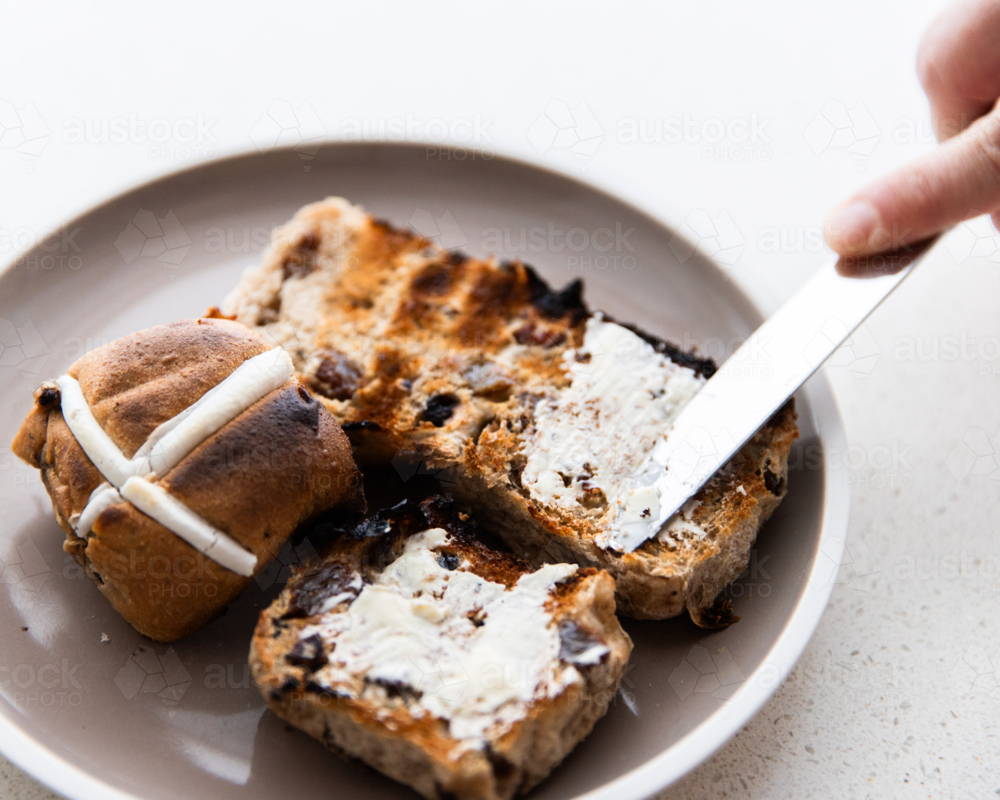 spreading butter on a freshly toasted hot cross bun - Australian Stock Image